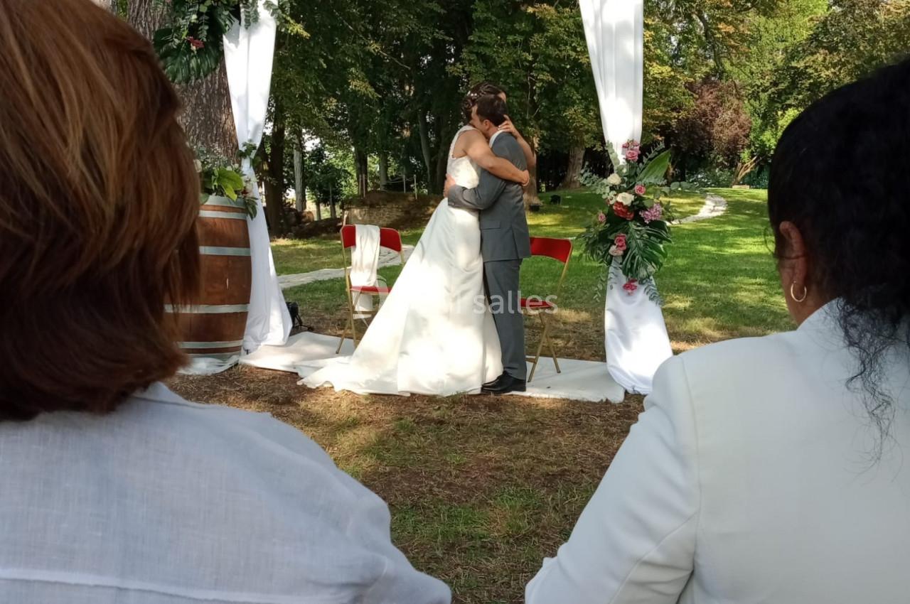 Un couple s'embrasse sous une arche décorée de fleurs lors d'une cérémonie de mariage en plein air.