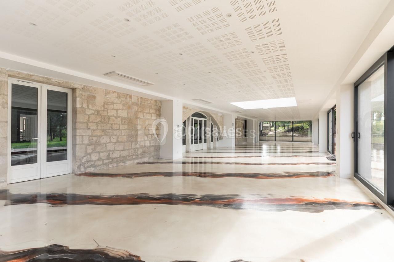 Salle lumineuse avec sol en résine aux motifs organiques, murs en pierre et grandes baies vitrées donnant sur un jardin.