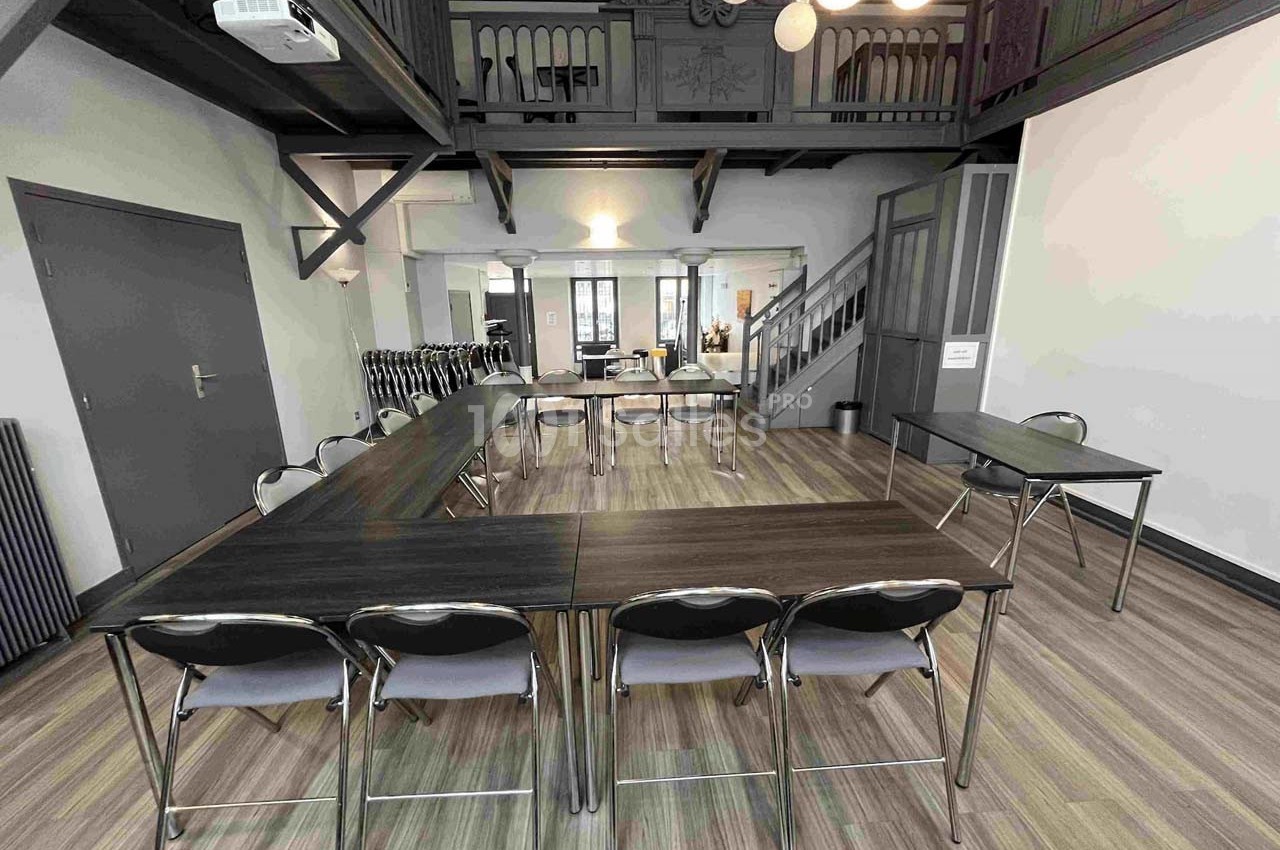 Salle de réunion lumineuse avec tables en U, chaises pliantes et mezzanine visible en arrière-plan.