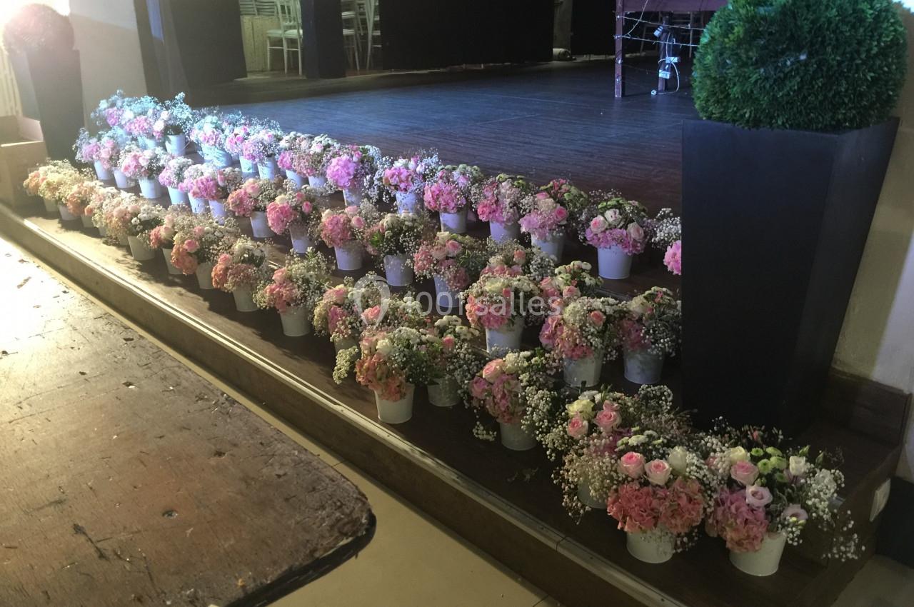 Alignement de petits bouquets de fleurs roses et blanches dans des pots blancs, disposés sur des marches en bois.