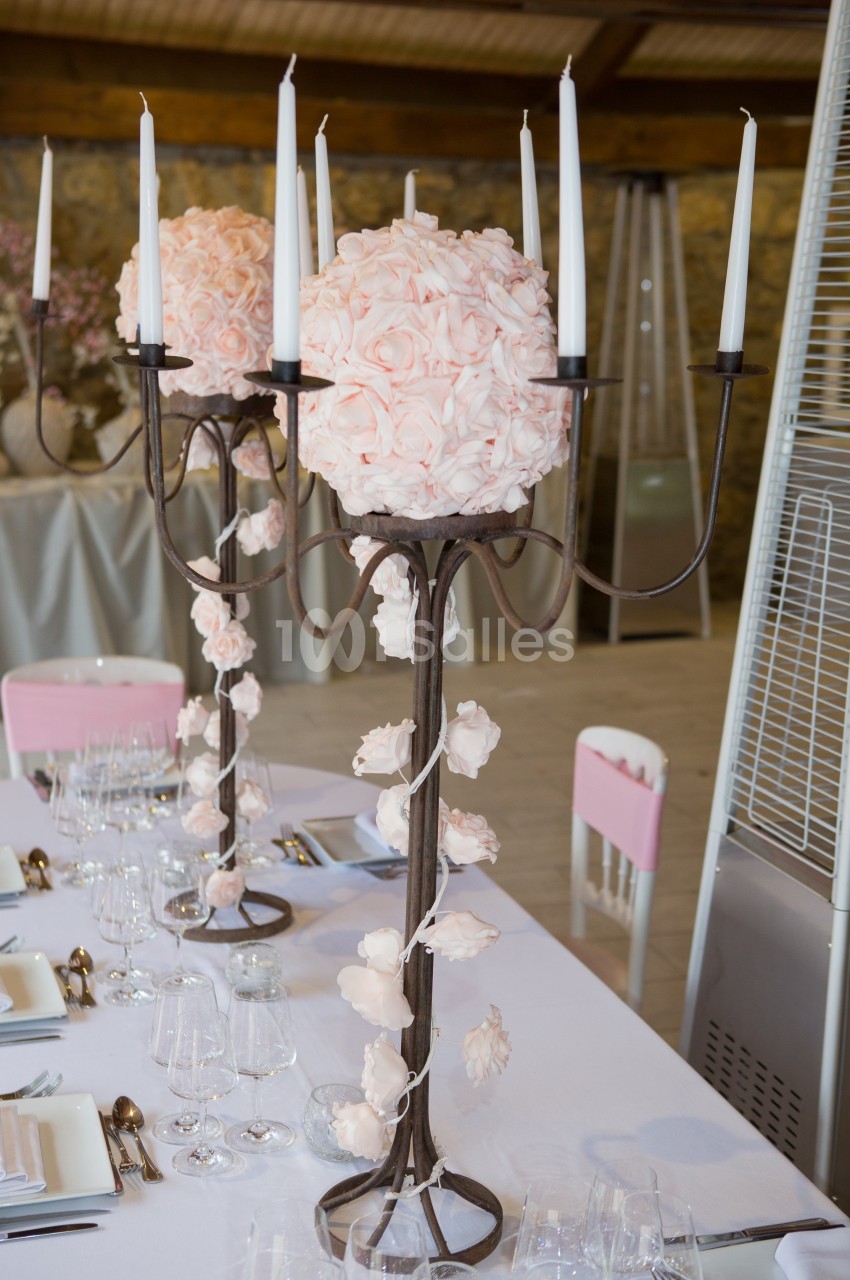 Centre de table avec chandelier noir orné de fleurs roses et bougies blanches, disposé sur une table dressée élégamment.