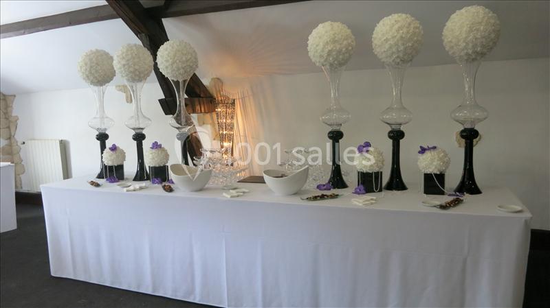 Table décorée avec des vases hauts contenant des boules de fleurs blanches, accompagnée de bols et d'éléments décoratifs.
