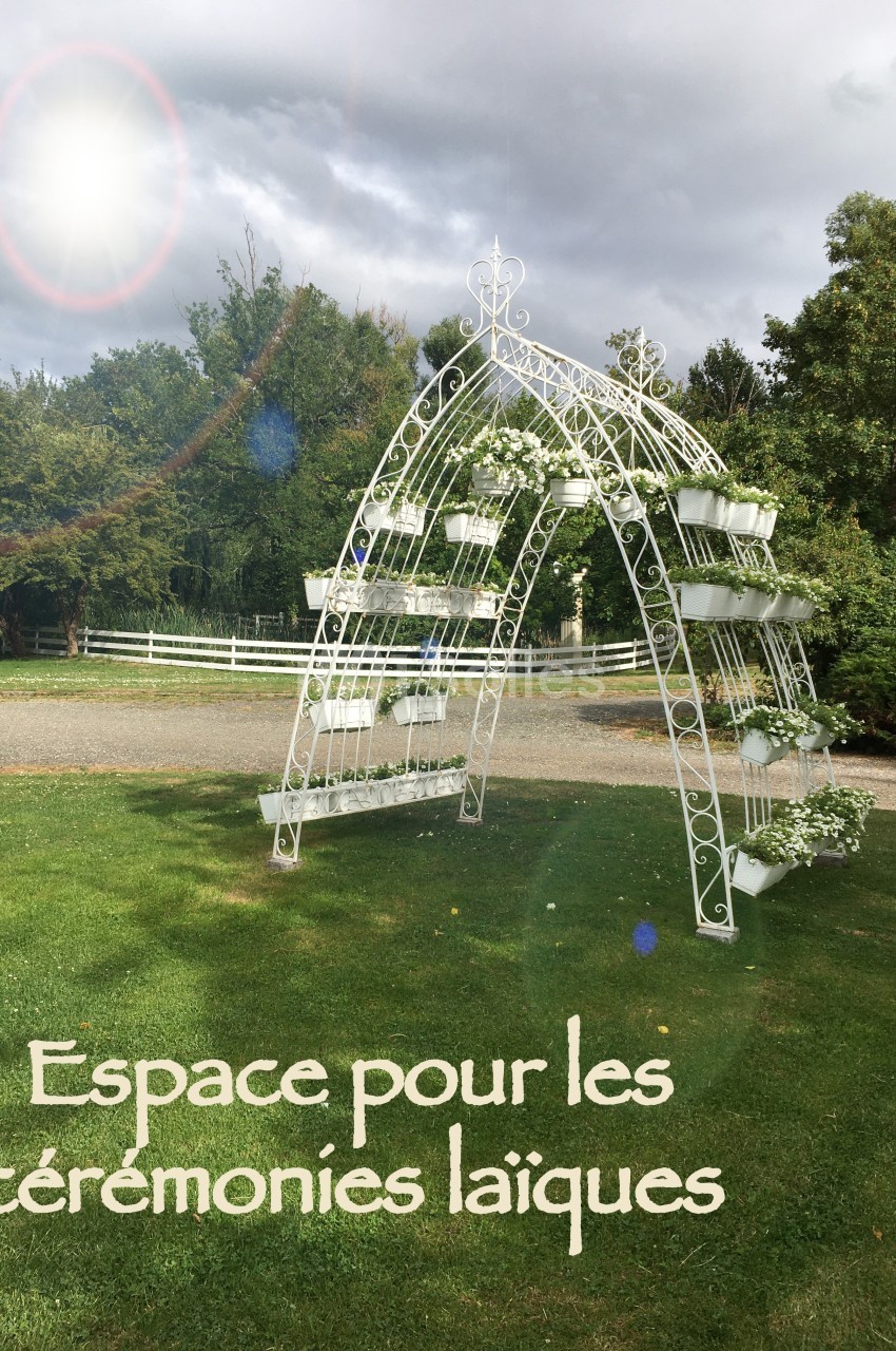 Arche blanche décorative en métal avec des fleurs blanches, installée sur une pelouse dans un jardin verdoyant.