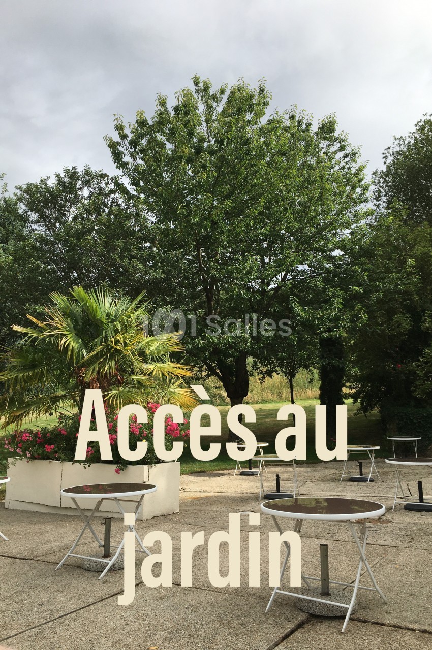 Espace extérieur avec tables, chaises et végétation, incluant des arbres et un palmier sous un ciel nuageux.