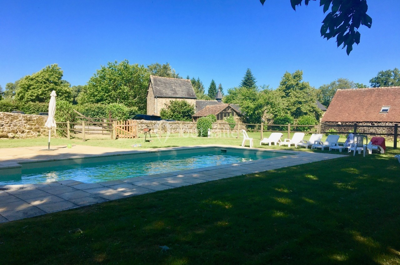 Piscine extérieure entourée de chaises longues, située dans un jardin avec des bâtiments en pierre et des arbres en arrière…