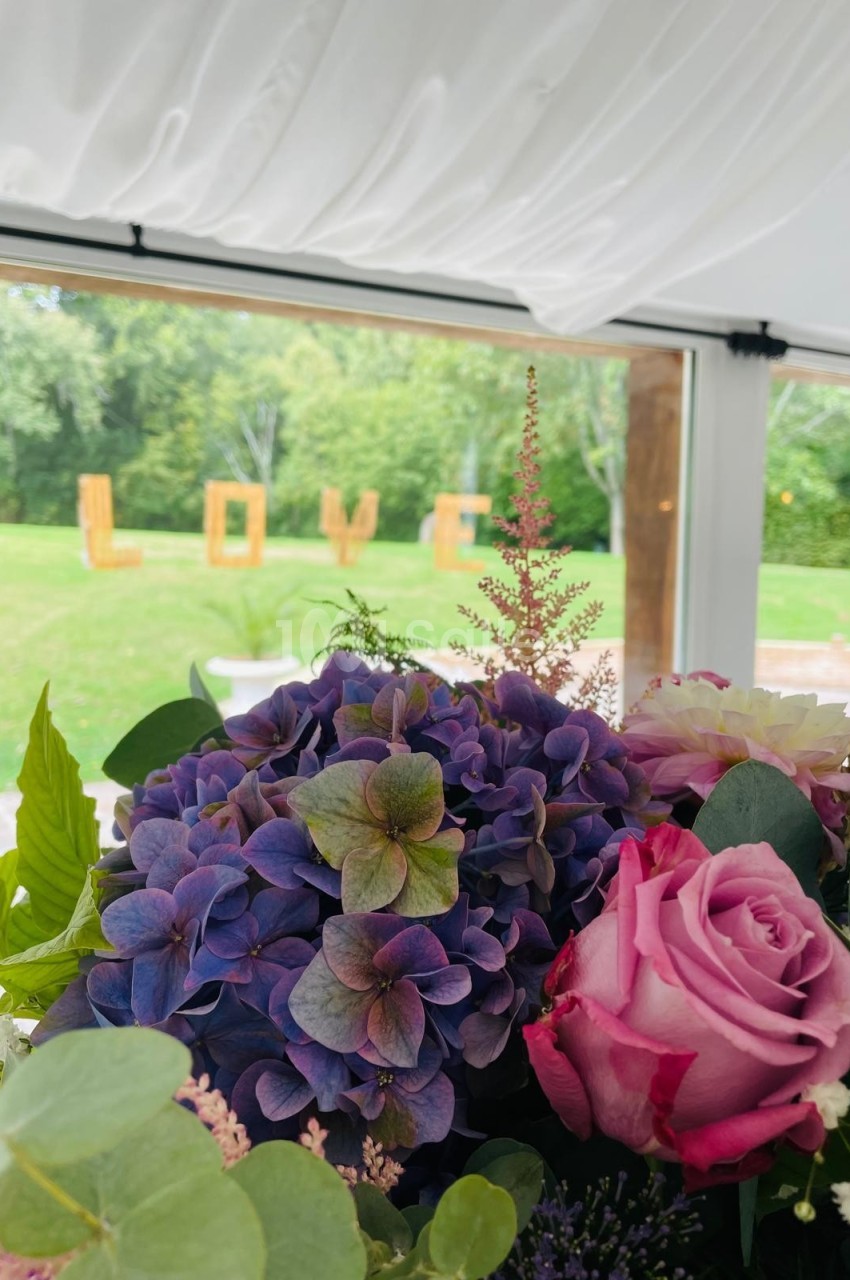 Bouquet de fleurs colorées au premier plan avec des lettres formant ’LOVE’ visibles à travers une fenêtre donnant sur un…