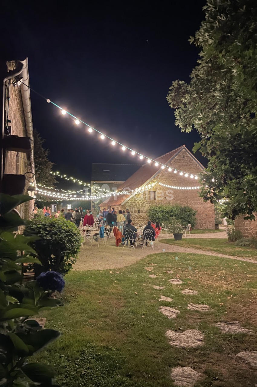 Cour extérieure éclairée par des guirlandes lumineuses, avec des invités rassemblés près de bâtiments en pierre.