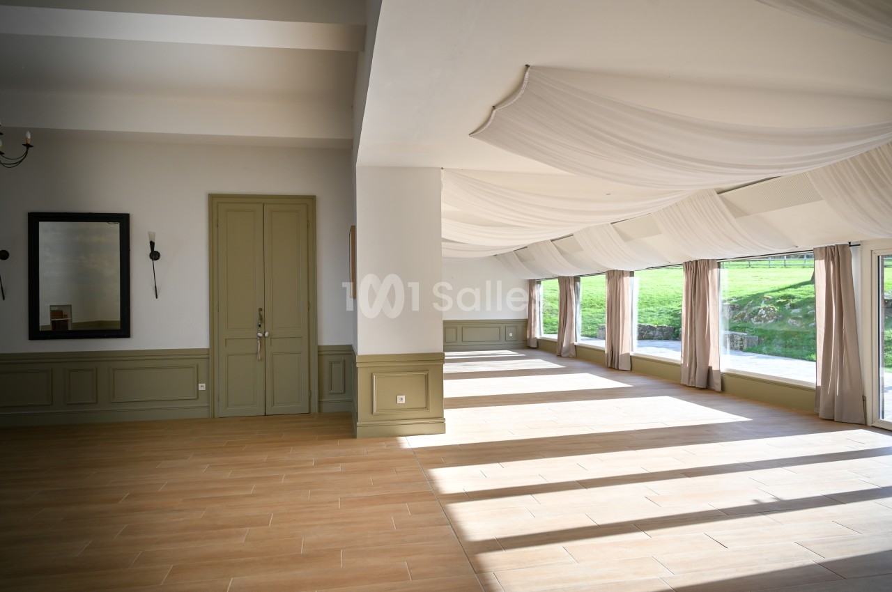 Salle lumineuse avec parquet clair, murs blancs et verts, grandes fenêtres donnant sur un espace extérieur verdoyant.