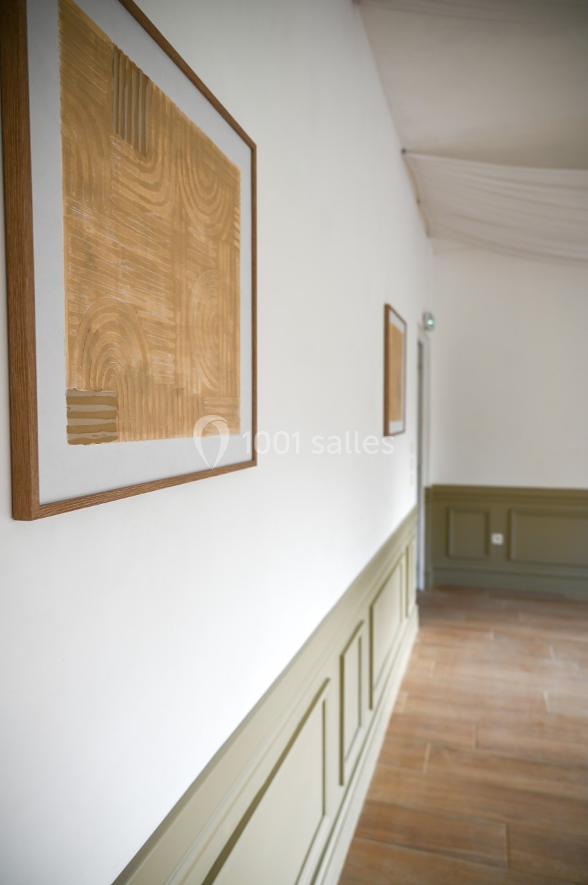 Tableau abstrait encadré accroché sur un mur blanc, dans un couloir avec un sol en bois et des moulures vertes.