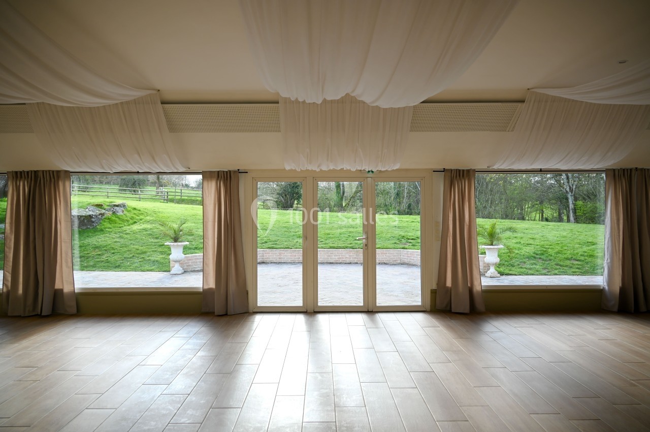 Salle lumineuse avec grandes baies vitrées donnant sur un jardin verdoyant, rideaux beiges et plafond décoré de voilages.