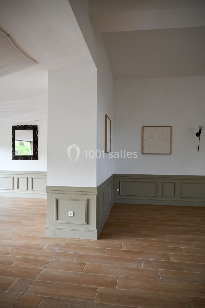 Mur blanc avec moulures vertes, sol en carrelage beige, deux cadres accrochés et un miroir noir en arrière-plan.
