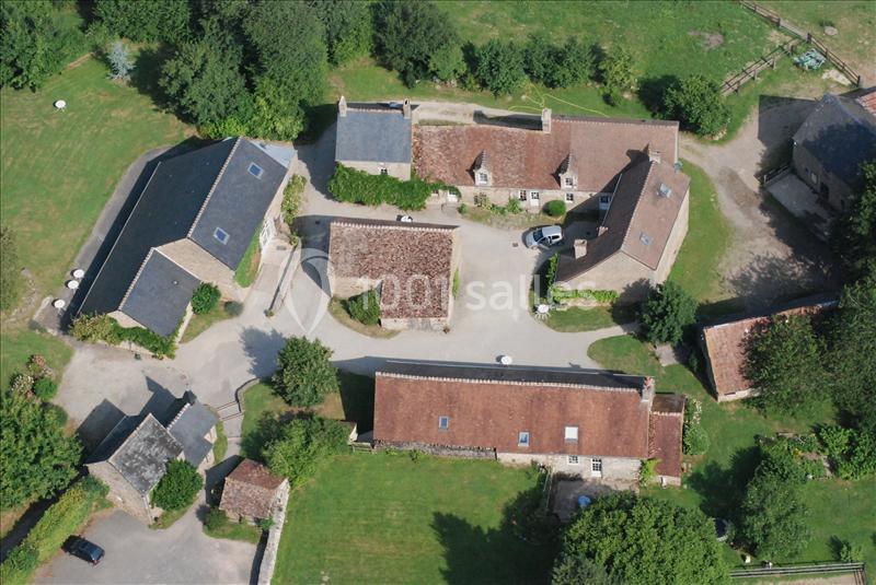 Vue aérienne d'un ensemble de bâtiments en pierre avec toits en tuiles et ardoises, entourés de verdure.