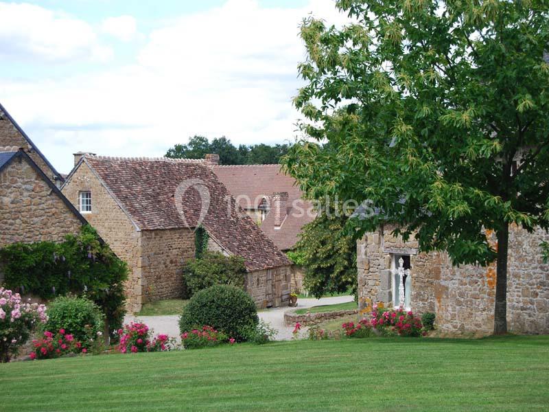 Maisons en pierre entourées de verdure et de fleurs dans un cadre rural sous un ciel partiellement nuageux.
