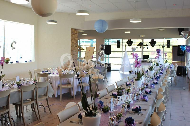Salle décorée pour un événement avec tables dressées, orchidées en centre de table et espace pour la danse au fond.