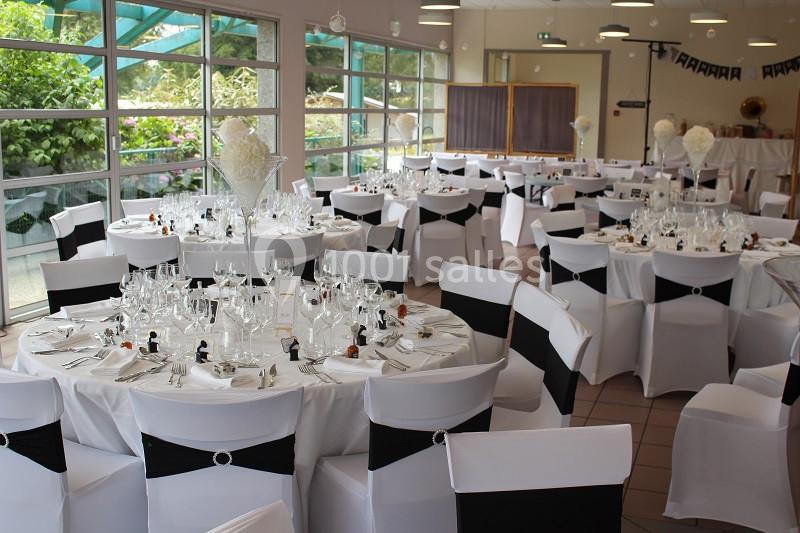 Salle de réception décorée avec des tables rondes dressées, nappes blanches et chaises ornées de nœuds noirs.