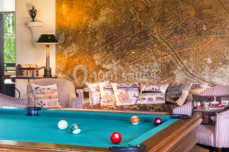 Location salle Gressy (Seine-et-Marne) - Le Manoir de Gressy #20 Table de billard avec des boules colorées au premier plan, entourée de fauteuils et d'une carte murale en arrière-plan.