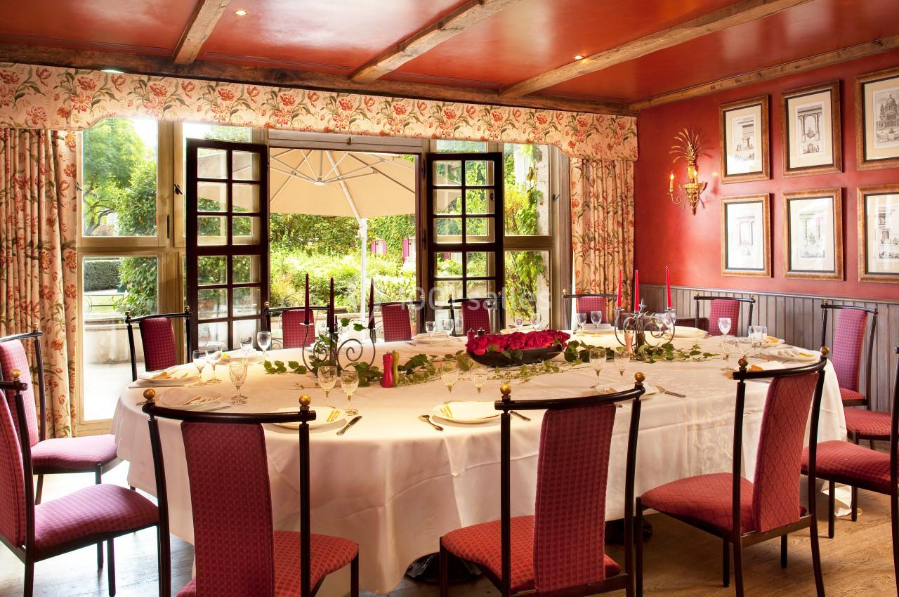 Location salle Gressy (Seine-et-Marne) - Le Manoir de Gressy #8 Salle à manger élégante avec une grande table dressée, entourée de chaises rouges, et vue sur un jardin par des fenêtres…