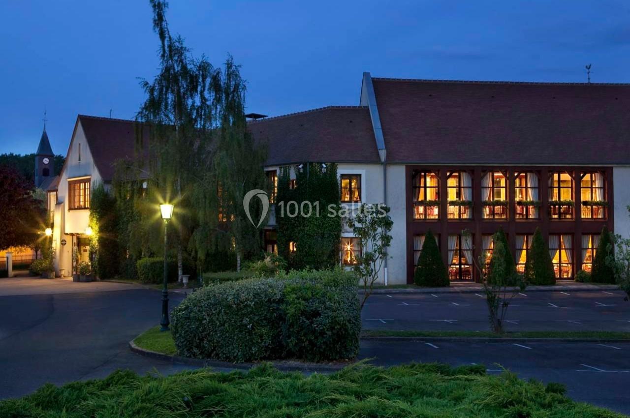 Location salle Gressy (Seine-et-Marne) - Le Manoir de Gressy #10 Façade d'un bâtiment éclairé à la tombée de la nuit, entouré de végétation et d'un parking partiellement visible.