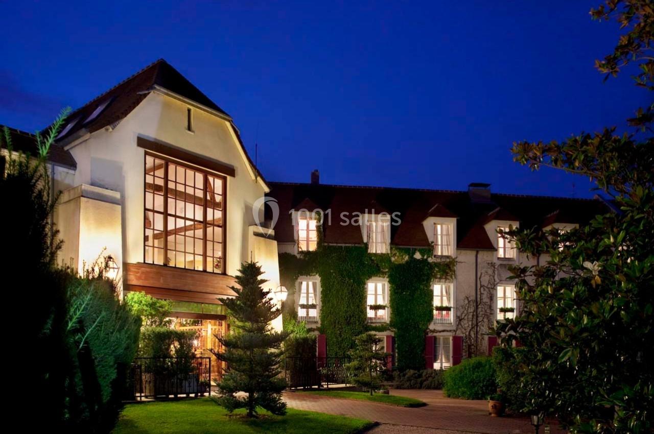 Location salle Gressy (Seine-et-Marne) - Le Manoir de Gressy #12 Façade d'un bâtiment éclairé de nuit, entouré de végétation et d'un chemin menant à l'entrée principale.