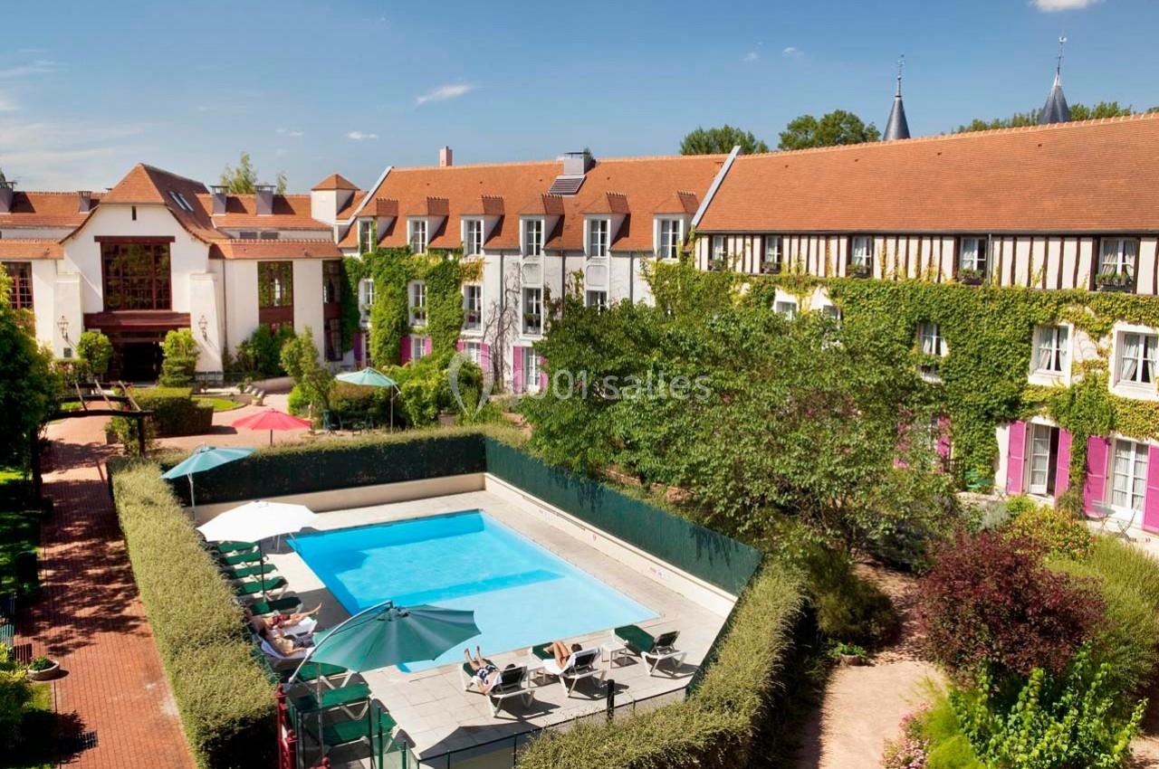 Location salle Gressy (Seine-et-Marne) - Le Manoir de Gressy #3 Vue aérienne d'un hôtel avec piscine extérieure, entouré de bâtiments aux toits en tuiles et de végétation.