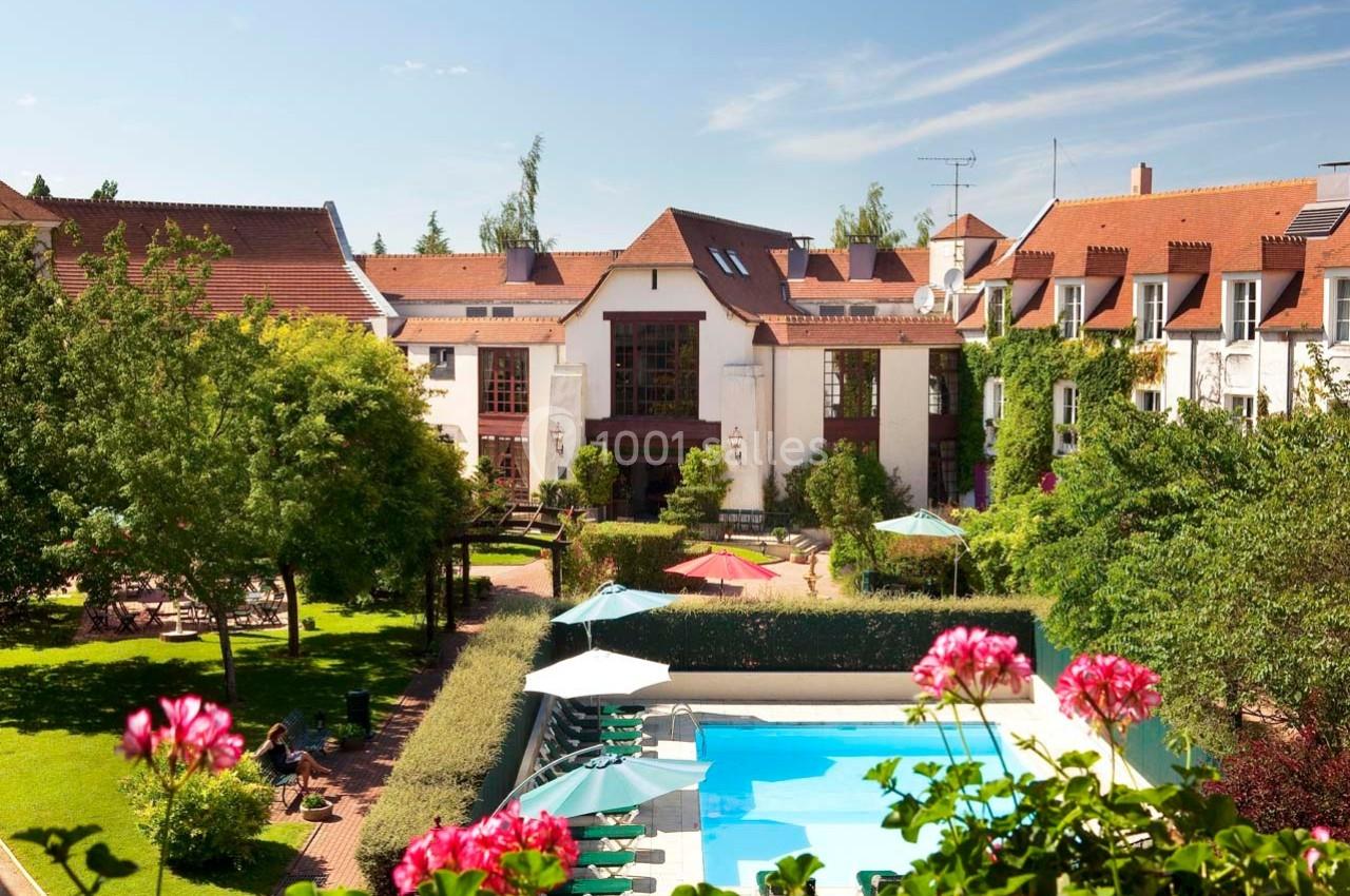 Location salle Gressy (Seine-et-Marne) - Le Manoir de Gressy #1 Vue d'un hôtel avec piscine extérieure, parasols, jardins verdoyants et bâtiments aux toits en tuiles rouges.