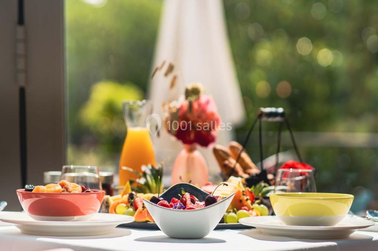 Location salle Gressy (Seine-et-Marne) - Le Manoir de Gressy #22 Table dressée avec des bols de fruits, un pichet de jus d'orange et des décorations florales en arrière-plan lumineux.