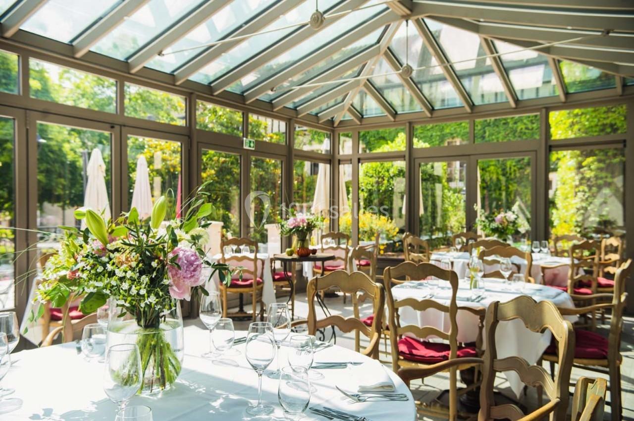 Location salle Gressy (Seine-et-Marne) - Le Manoir de Gressy #4 Salle lumineuse avec verrière, tables dressées avec nappes blanches, chaises en bois et bouquets de fleurs.