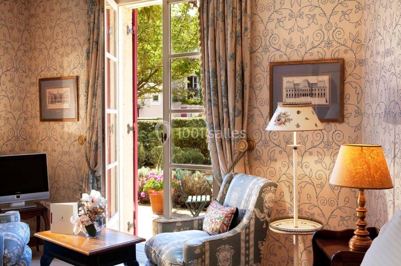 Location salle Gressy (Seine-et-Marne) - Le Manoir de Gressy #25 Salon lumineux avec fauteuils, table basse, lampe et fenêtre ouverte donnant sur un jardin verdoyant.