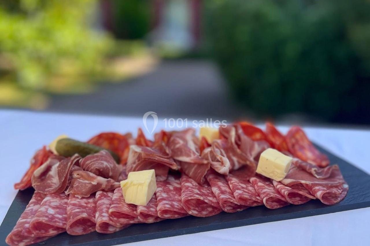 Location salle Gressy (Seine-et-Marne) - Le Manoir de Gressy #19 Plateau de charcuterie variée avec tranches de saucisson, jambon, fromage et cornichon, présenté sur une table en extérieur.