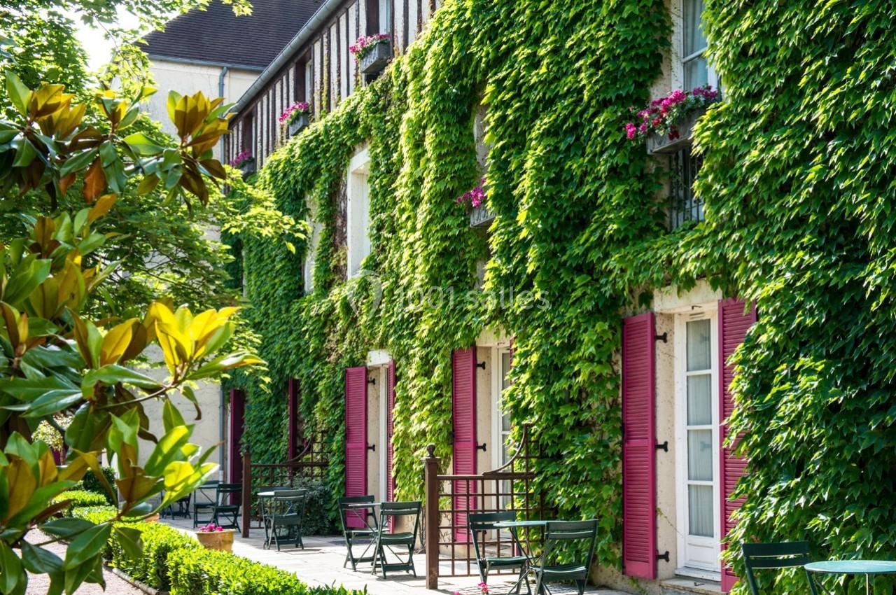 Location salle Gressy (Seine-et-Marne) - Le Manoir de Gressy #9 Façade d'un bâtiment recouverte de lierre avec volets roses, terrasses aménagées et végétation environnante.