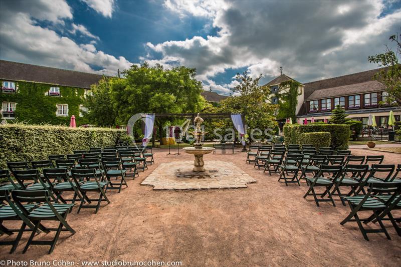 Location salle Gressy (Seine-et-Marne) - Le Manoir de Gressy #5 Chaises disposées en rangées face à une fontaine dans une cour extérieure entourée de bâtiments et de végétation.