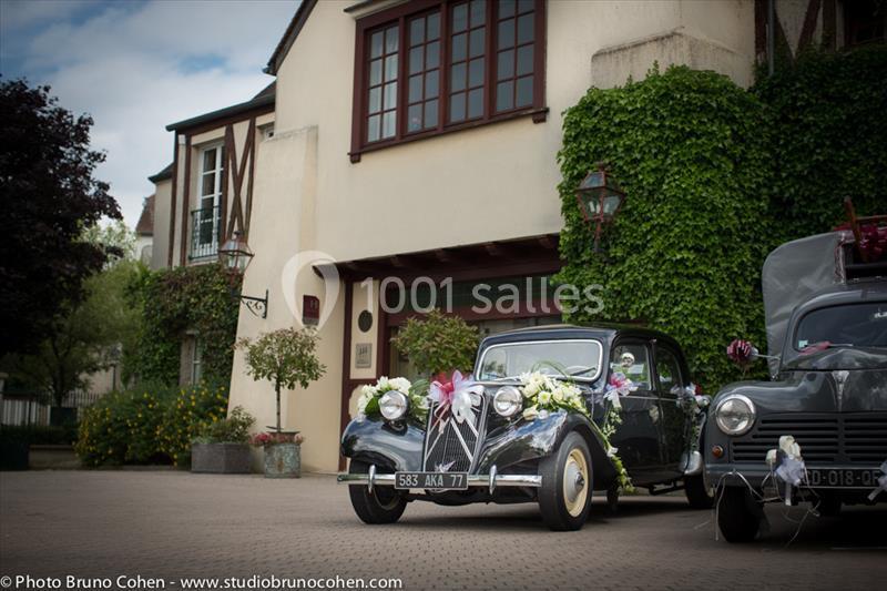 Location salle Gressy (Seine-et-Marne) - Le Manoir de Gressy #13 Voiture ancienne décorée de fleurs garée devant une maison avec façade en lierre et colombages.