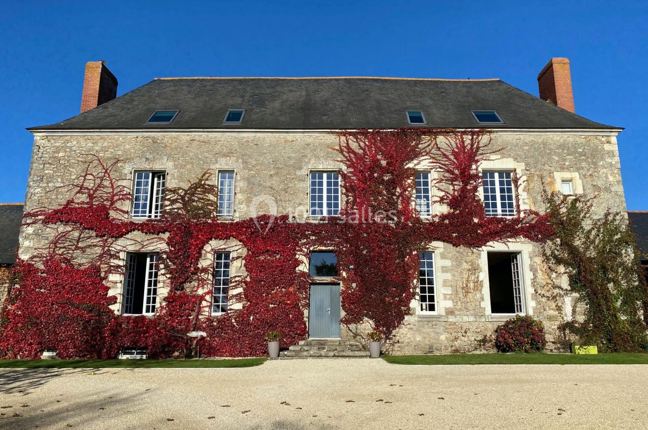 Façade d'une maison en pierre recouverte partiellement de vigne rouge, avec un ciel bleu en arrière-plan.