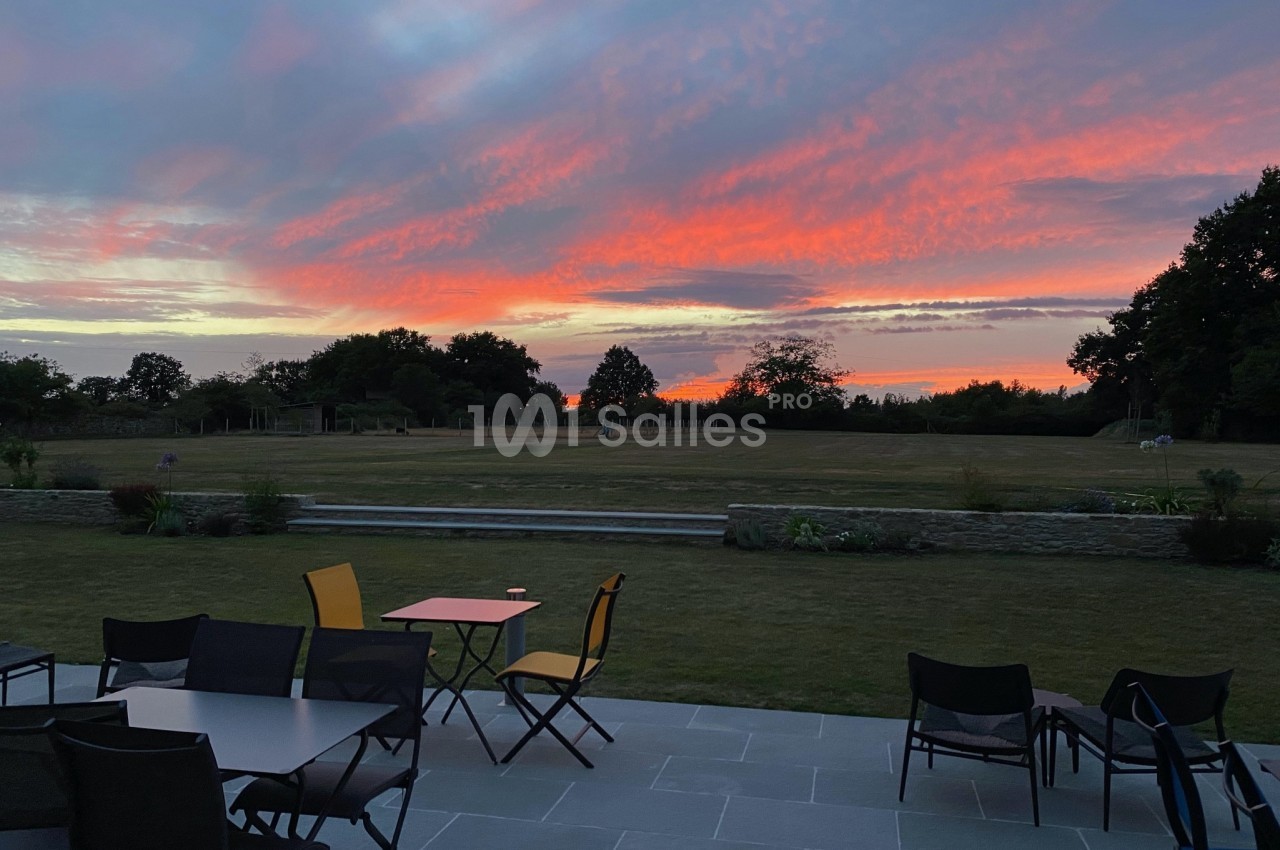 Ciel aux teintes rouges et roses au coucher du soleil, vu depuis une terrasse avec des tables et des chaises.