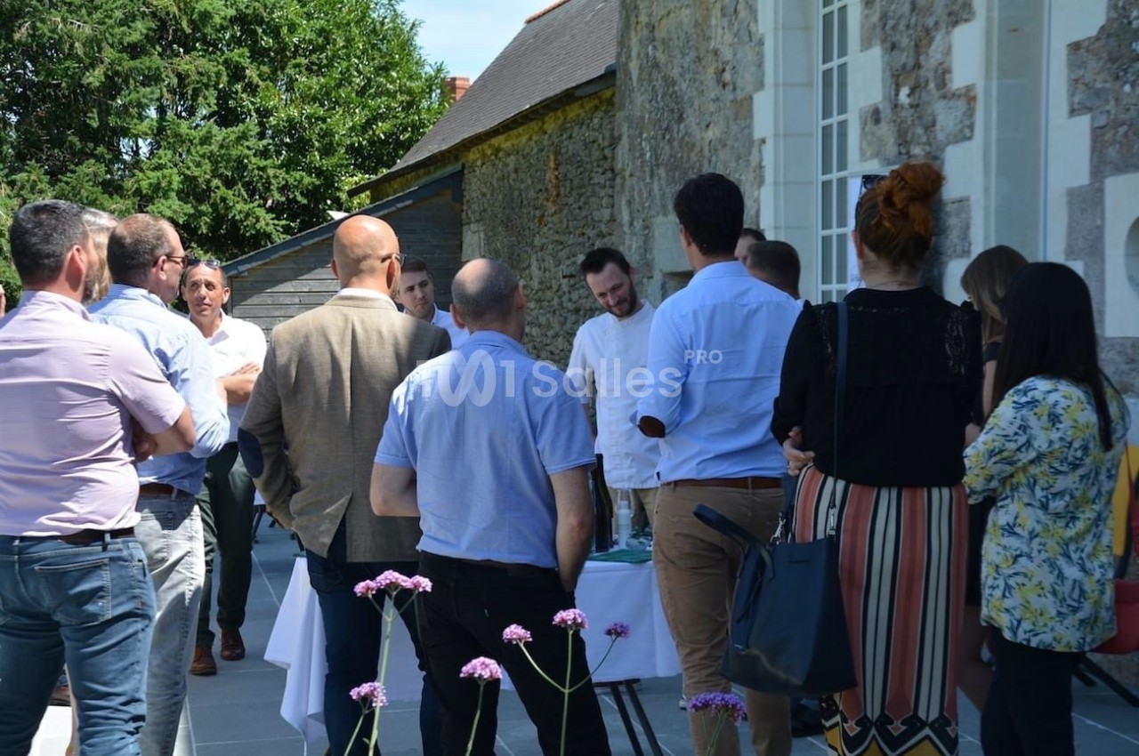 Un groupe de personnes discute en extérieur près d'une table, devant un bâtiment en pierre.