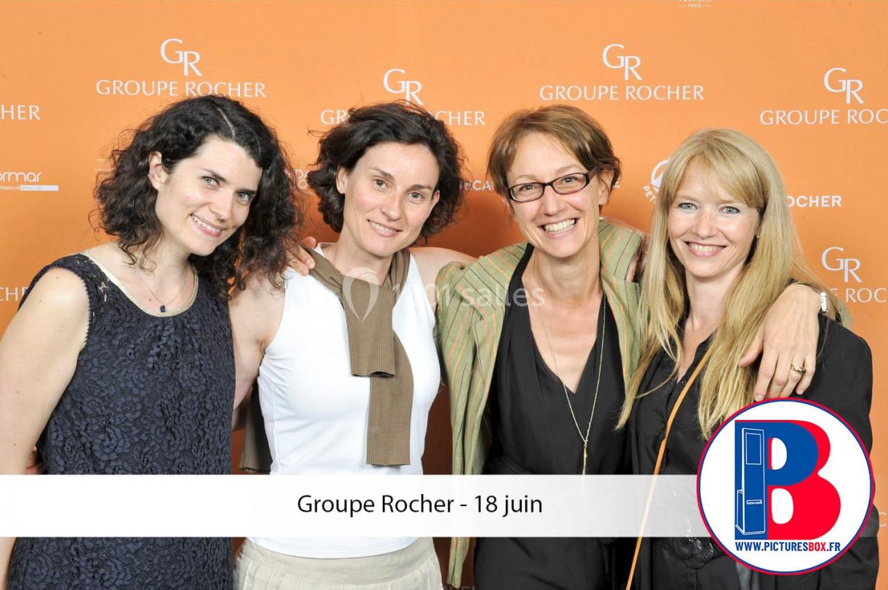 Quatre femmes souriantes posent devant un fond orange marqué ’Groupe Rocher’.