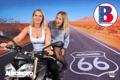 Deux femmes posent devant un décor de route désertique avec une moto et un logo ’AutomoTo 66’.