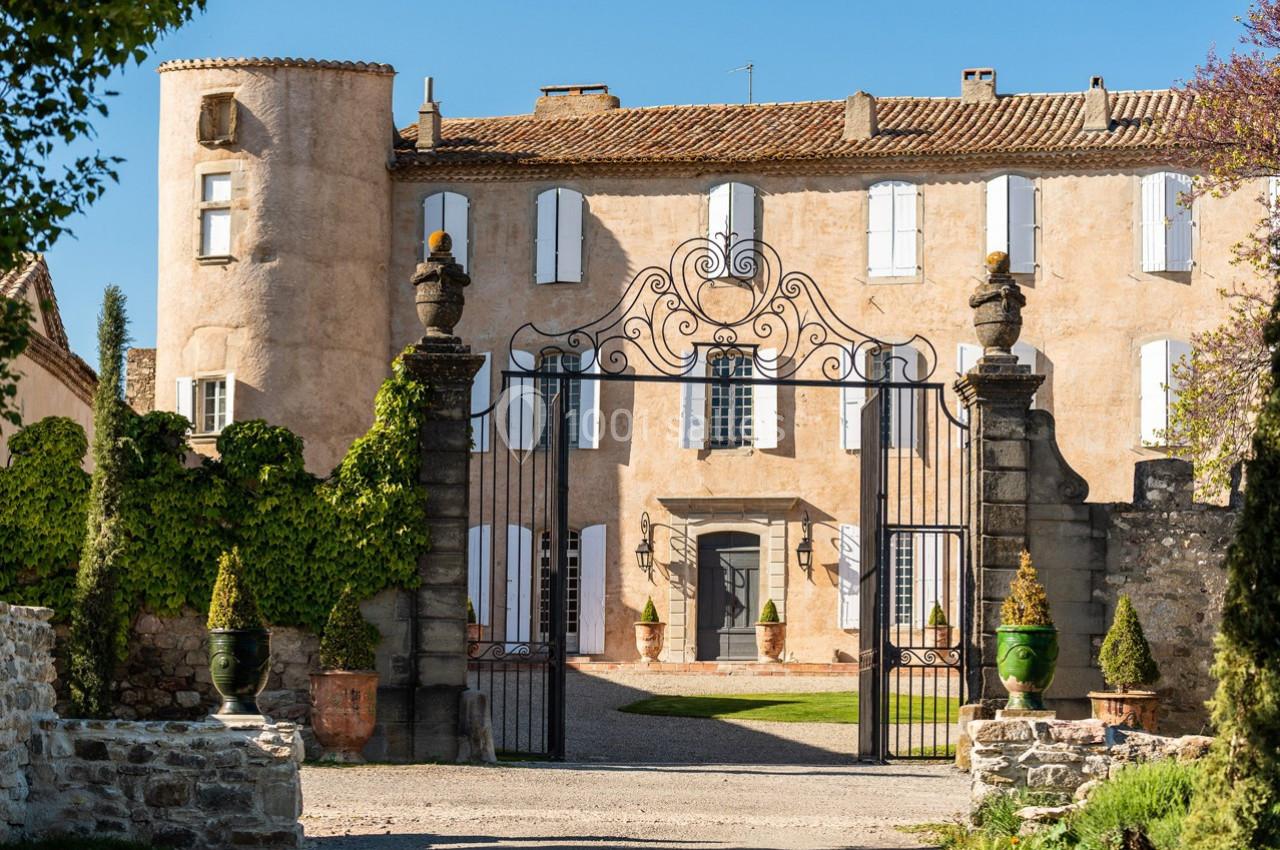 Façade d'un château ancien avec des volets blancs, une grille en fer forgé et un jardin à l'avant.