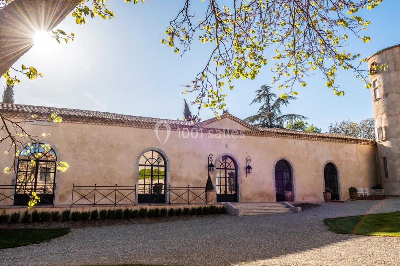 Façade d'un bâtiment en pierre avec grandes fenêtres cintrées, entouré d'arbres et baigné de lumière naturelle.