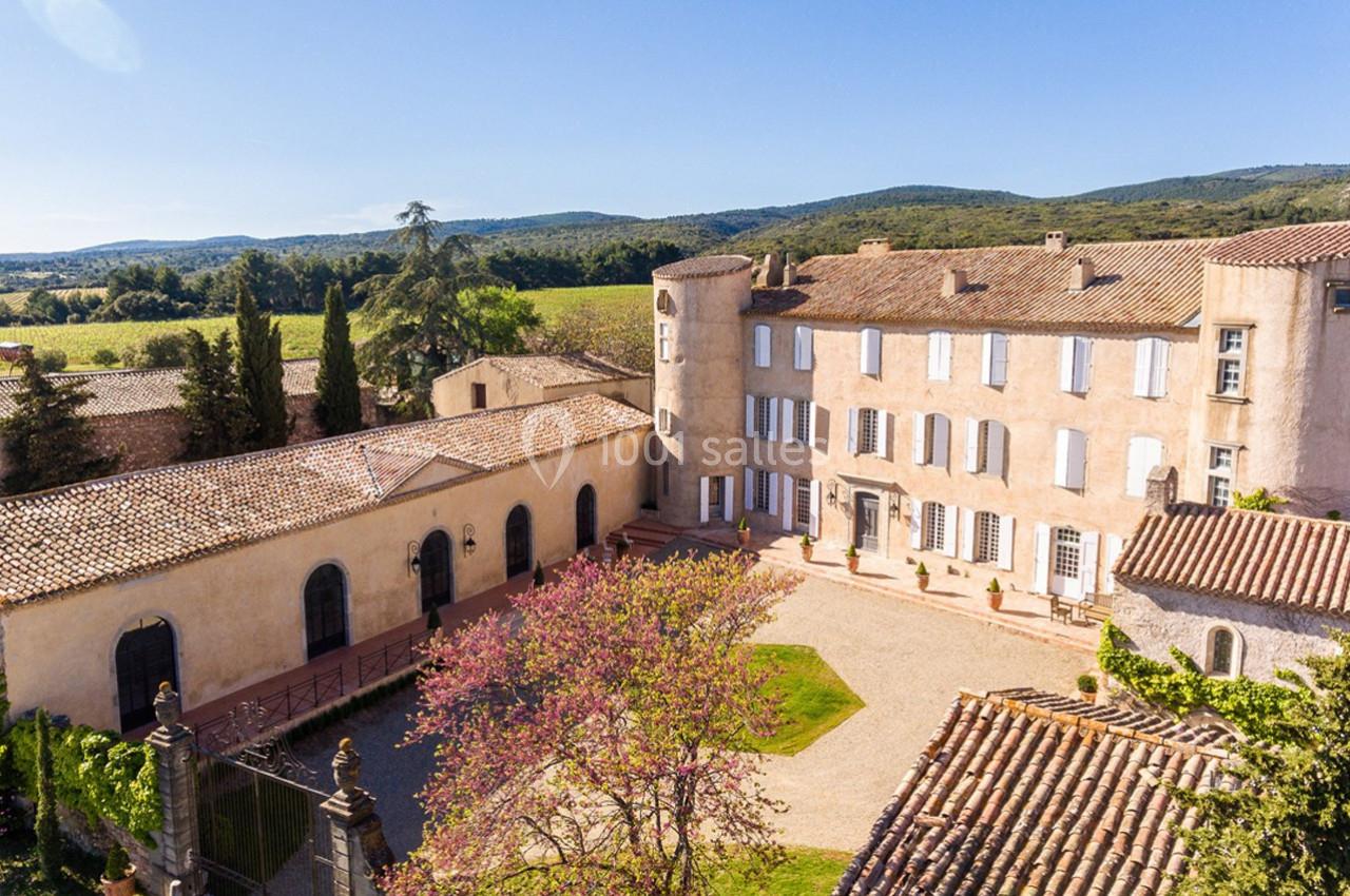 Vue aérienne d'un domaine avec un bâtiment historique, une cour centrale et des collines verdoyantes en arrière-plan.