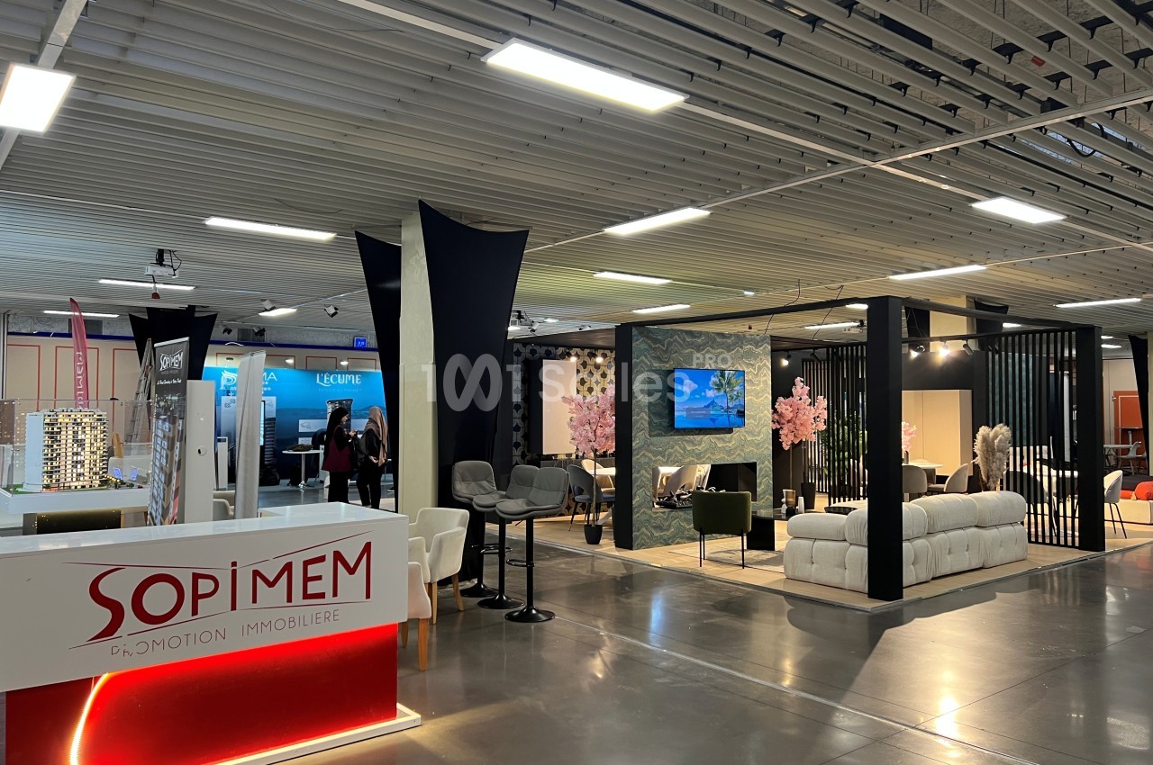 Vue d'un espace d'exposition avec stands aménagés, mobilier moderne et éclairage intérieur.