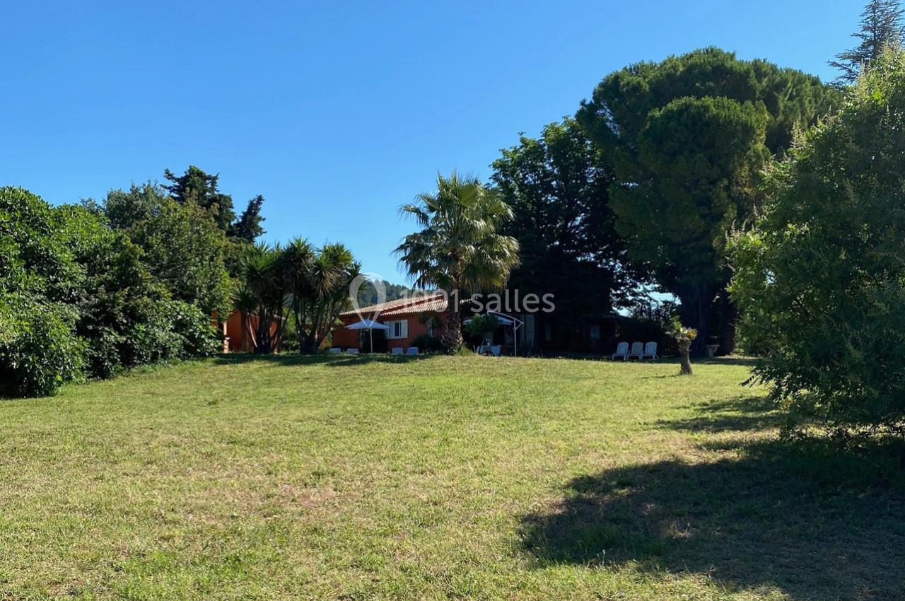 Pelouse verdoyante avec une maison entourée d'arbres et de palmiers sous un ciel bleu dégagé.