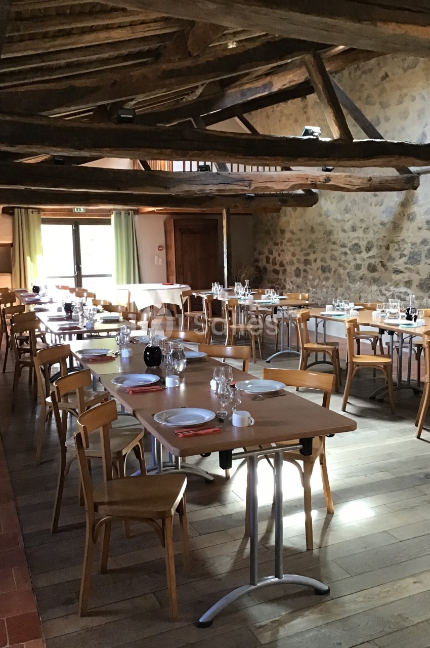 Salle à manger lumineuse avec tables en bois dressées, poutres apparentes et murs en pierre.
