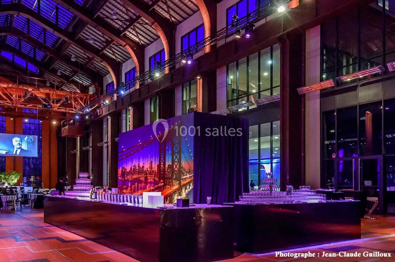 Salle de réception spacieuse avec éclairage coloré, grande table de buffet et décor urbain en arrière-plan.