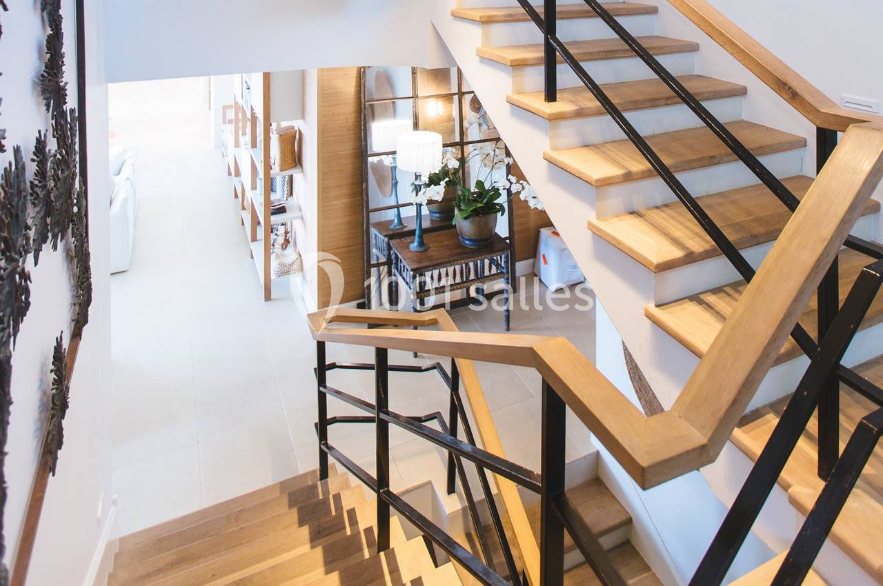 Escalier en bois avec garde-corps en métal noir, menant à un espace lumineux avec mobilier moderne et décoration épurée.
