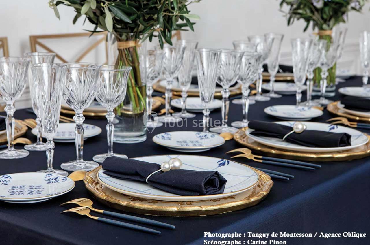 Table élégamment dressée avec nappes noires, vaisselle blanche et dorée, couverts dorés et verres en cristal.