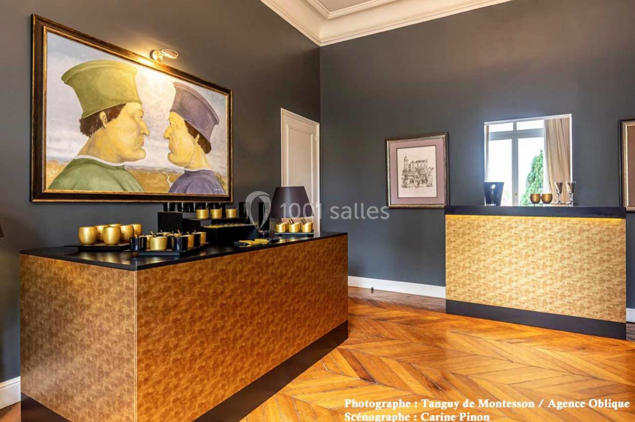 Salle élégante avec parquet en bois, comptoirs dorés, tableau mural et lumière naturelle entrant par une fenêtre.