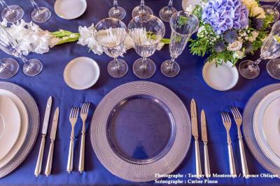 Salle lumineuse avec parquet en bois, table ronde dressée avec nappe rouge, et moulures décoratives au plafond.
