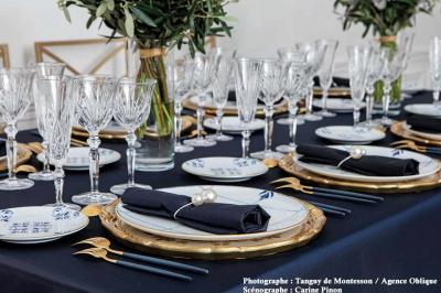 Espace salon moderne avec fauteuils verts, tables basses en bois, tapis rond clair, plantes et décorations murales.