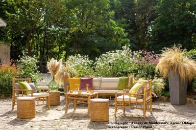 Espace salon moderne avec fauteuils verts, tables basses en bois, tapis rond clair, plantes et décorations murales.